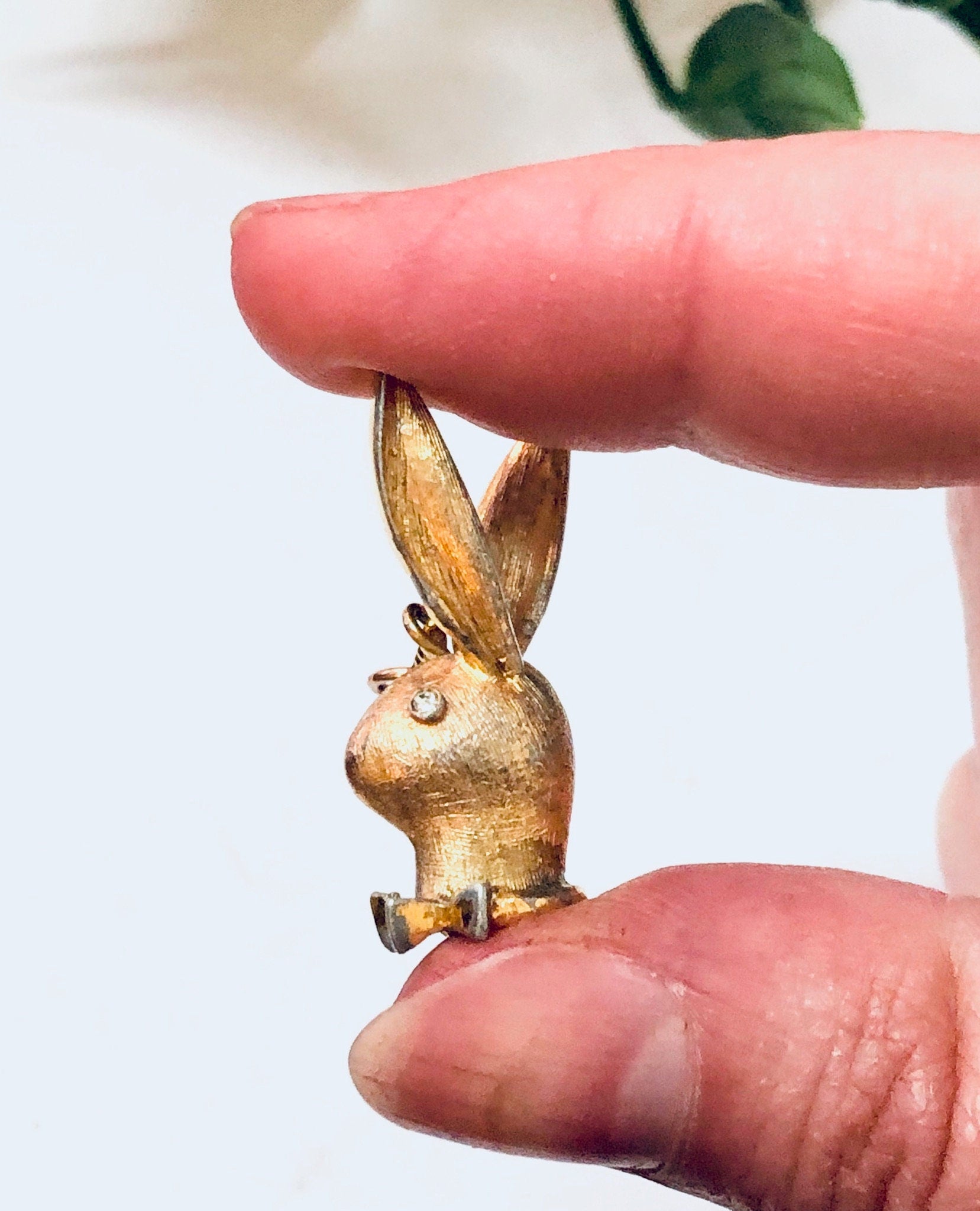 Vintage gold-toned Playboy bunny rabbit dangle pendant charm held between thumb and forefinger