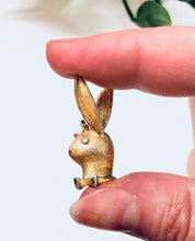 Vintage gold-toned Playboy bunny rabbit dangle pendant charm held between thumb and forefinger
