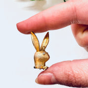 Vintage gold-toned Playboy bunny rabbit pendant charm held between fingers