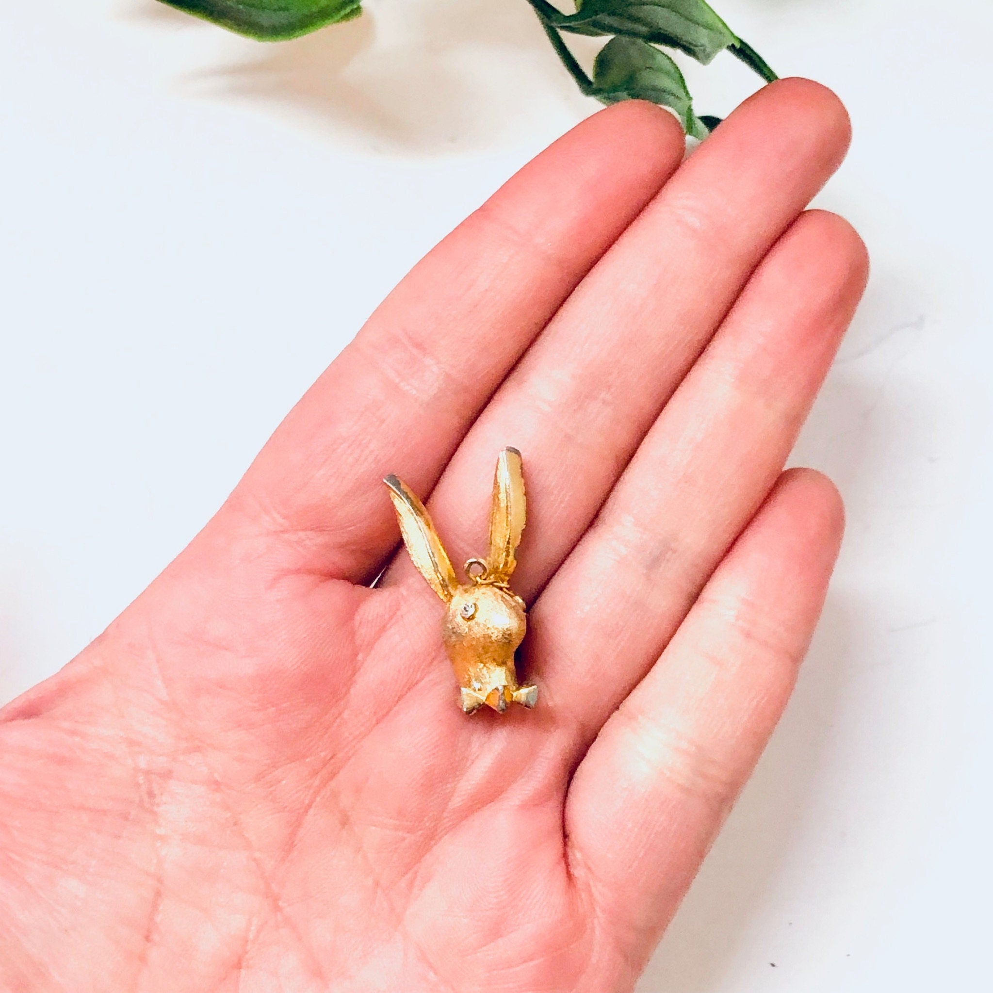 Vintage gold-toned Playboy bunny pendant charm held in palm of hand against white background.