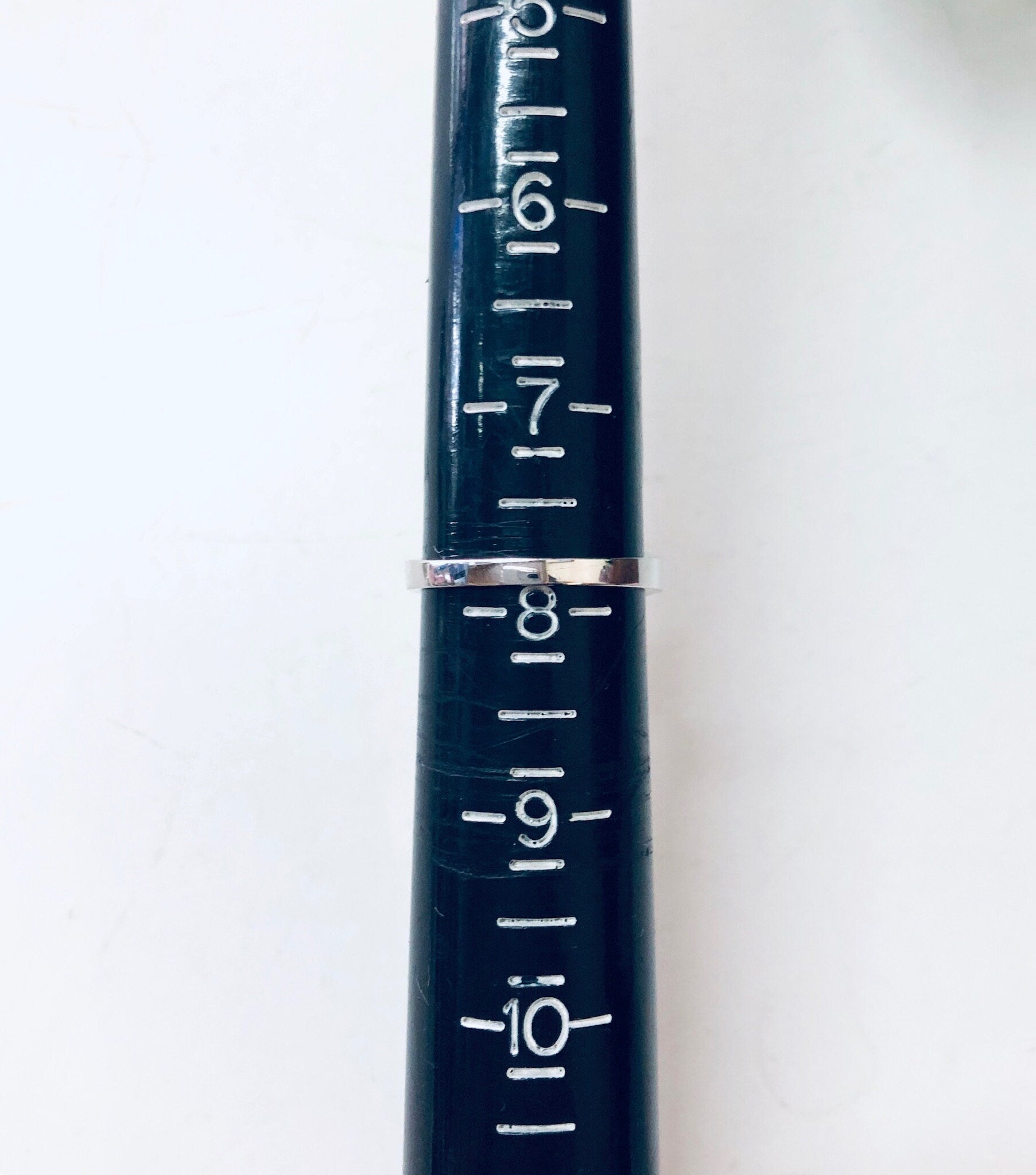 Close-up view of a blue vintage measuring ruler or rain gauge with silver markings indicating inches or centimeters against a plain white background.