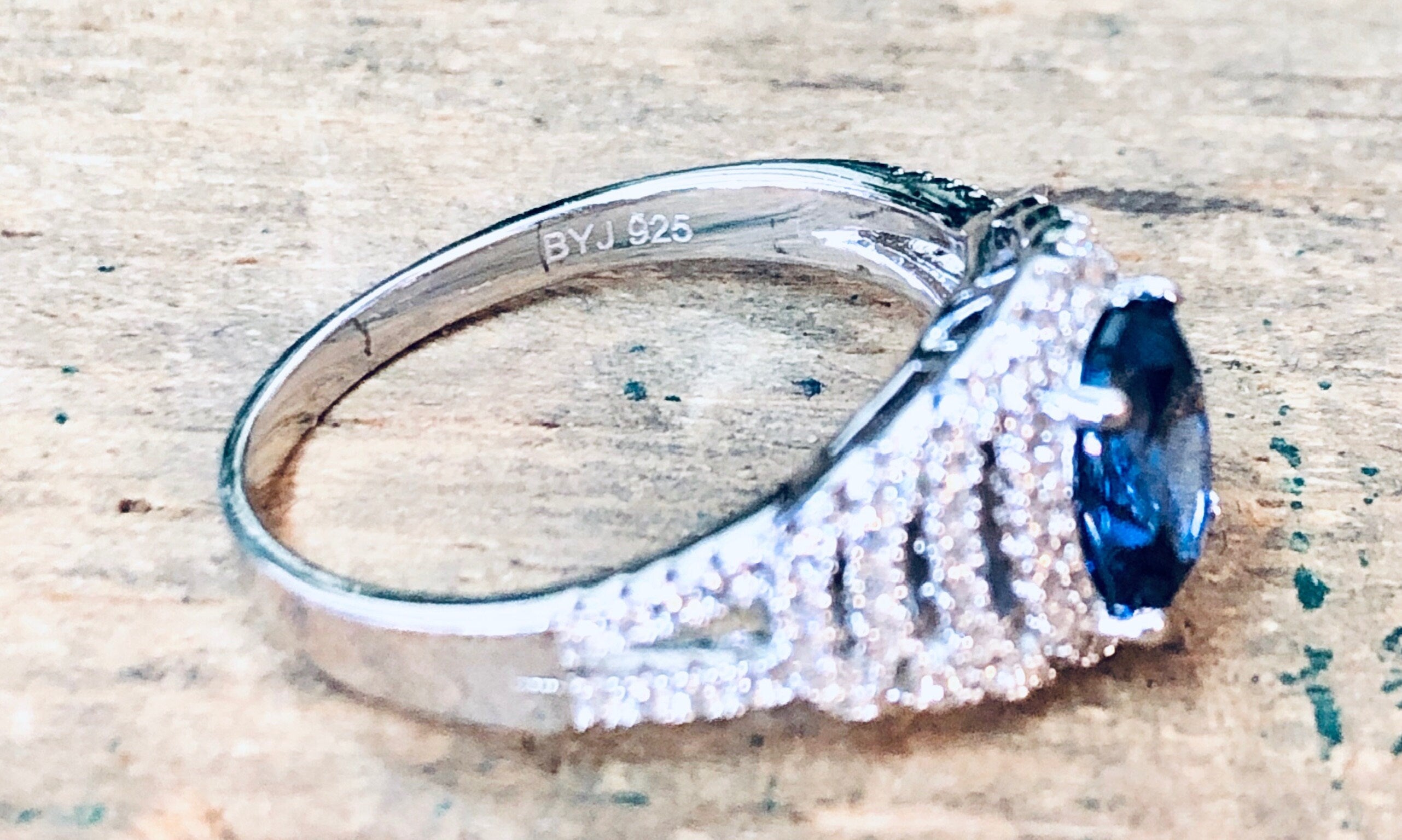 Vintage silver ring with blue stone and faux diamonds, marked "BYJ 925", on textured background
