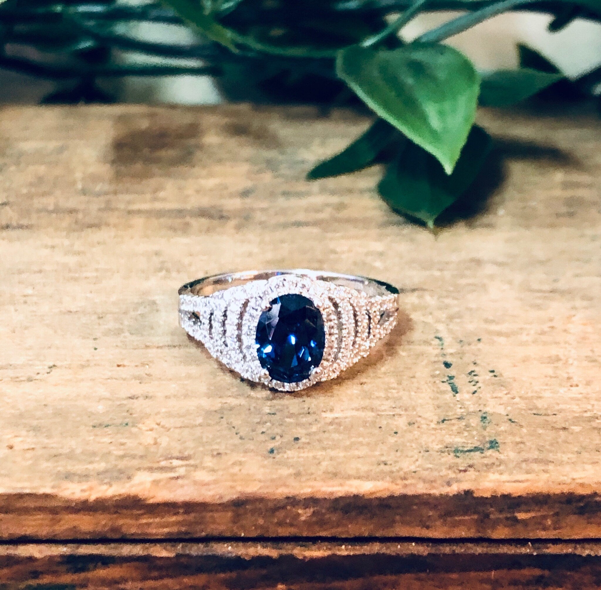 Vintage silver ring with blue stone and faux diamond accents on wooden surface with greenery in background