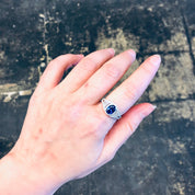 Vintage silver ring with blue stone and faux diamonds on hand against concrete background