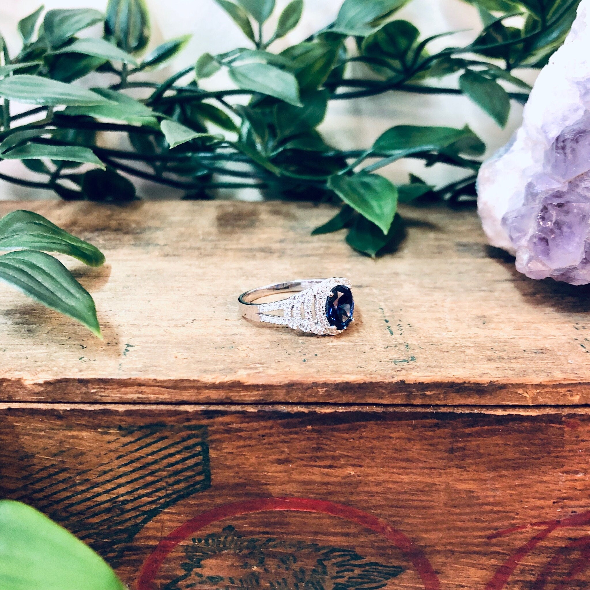 Vintage silver BYJ 925 ring with blue faux diamond stone on wooden surface surrounded by green leaves