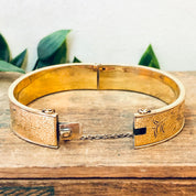 Vintage gold-filled bangle bracelet with etched floral design, displayed on wooden surface with leaves in background.