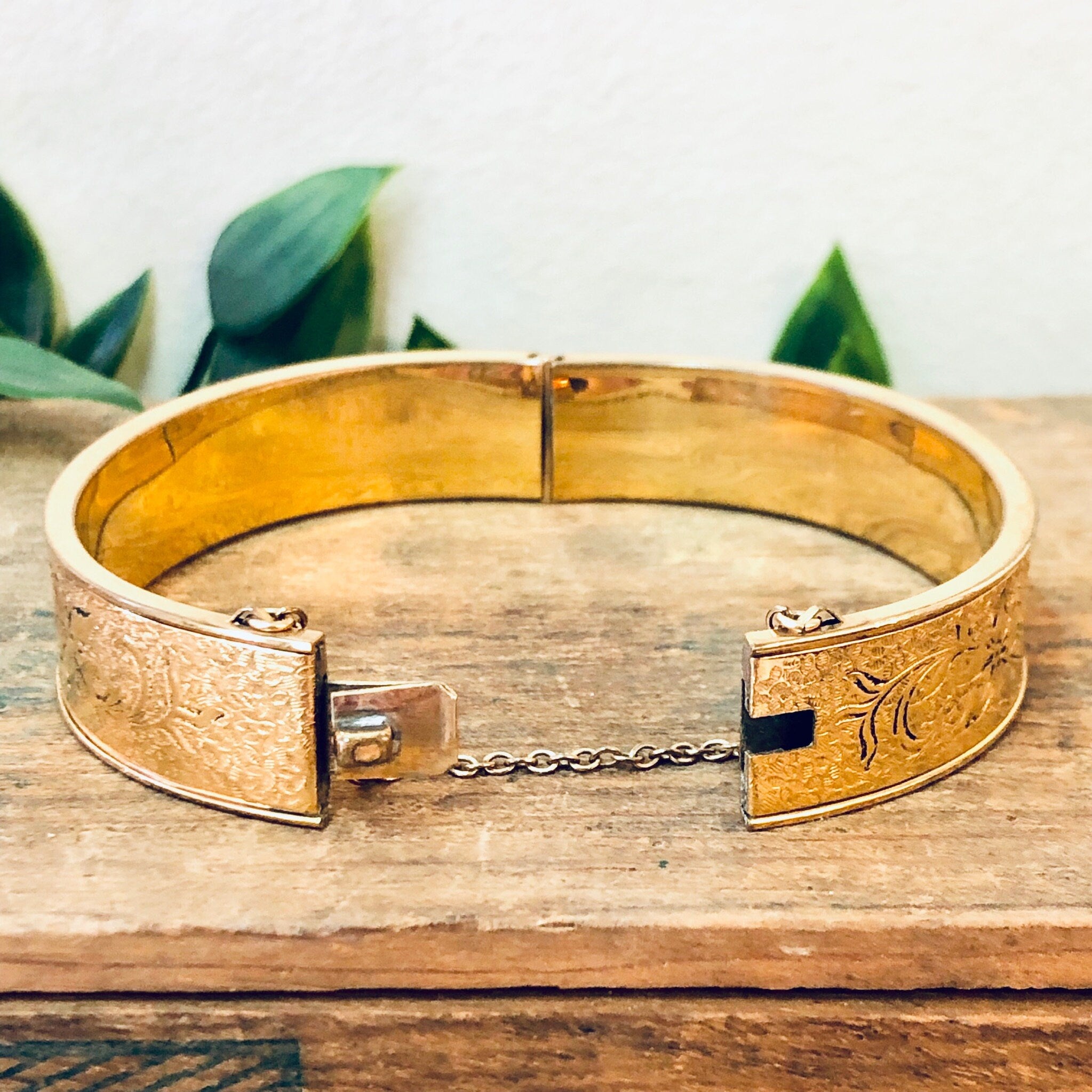 Vintage gold-filled bangle bracelet with etched floral design, displayed on wooden surface with leaves in background.