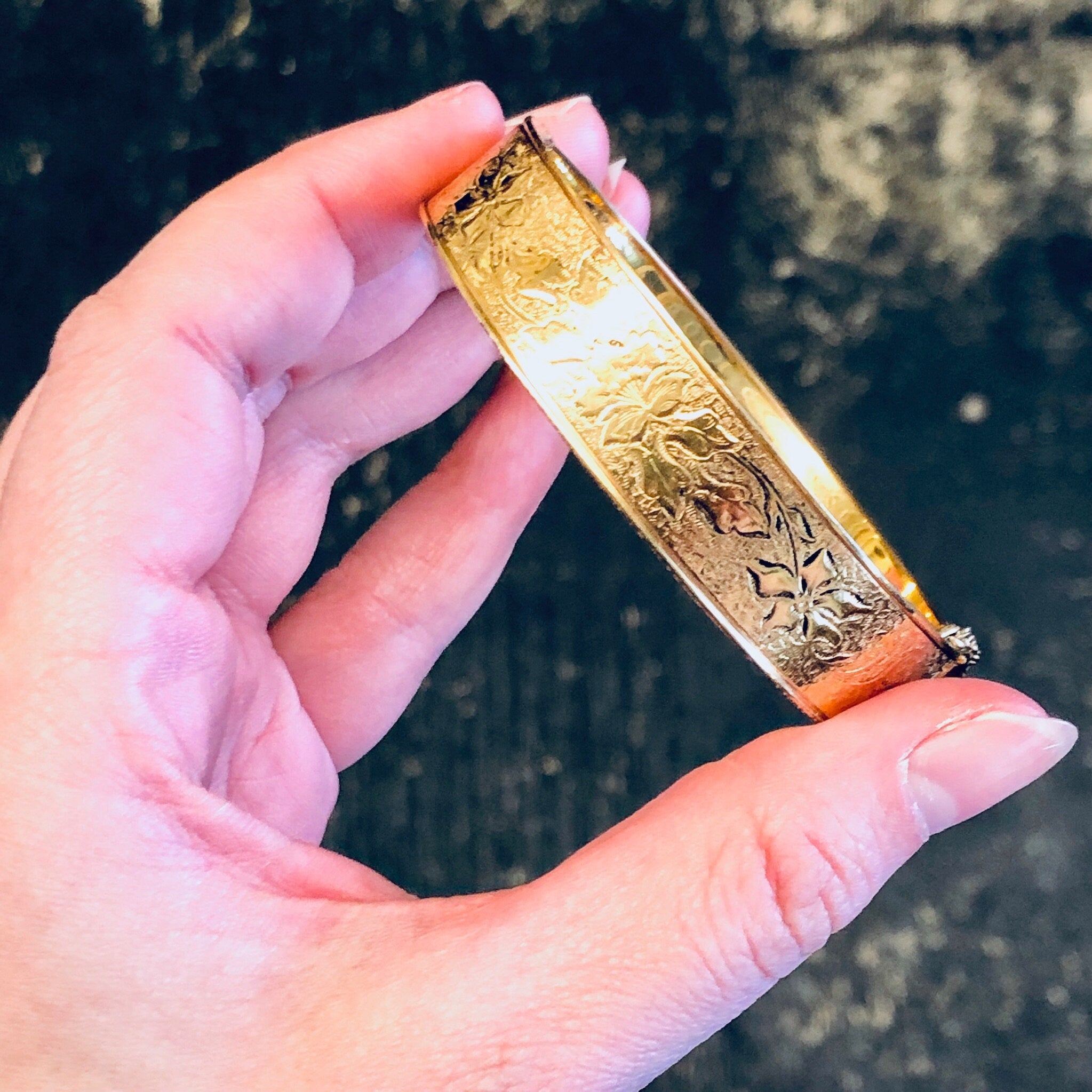 Vintage gold filled bangle bracelet with intricate etched floral design held in hand.