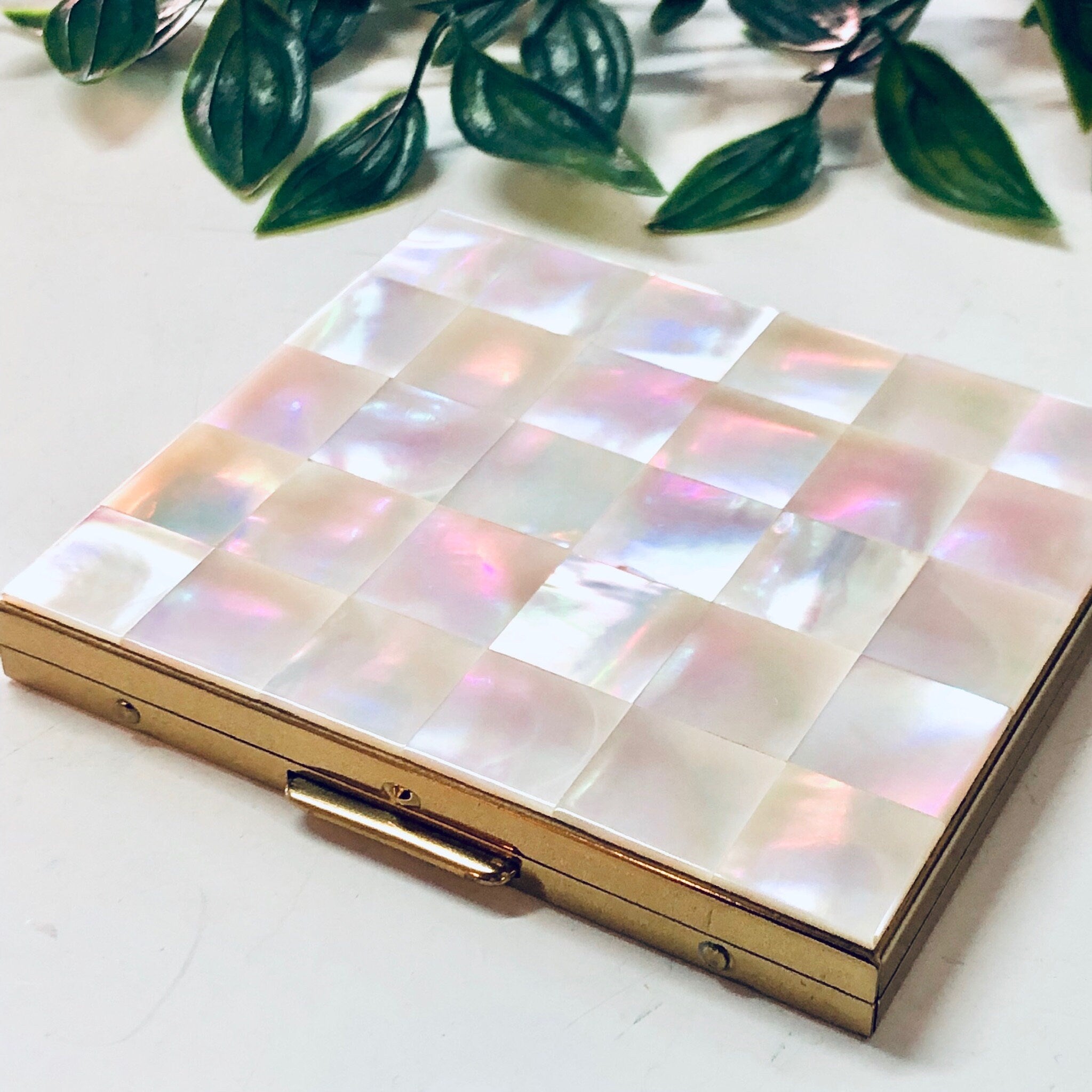 Vintage mother of pearl cigarette case or business card holder from Bailey Banks and Biddle, featuring an iridescent pink checkered design, displayed with green leaves.