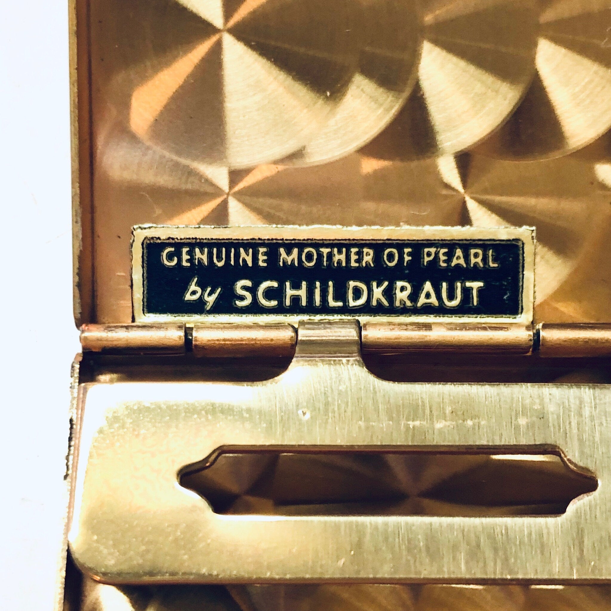 Vintage gold cigarette case with "Genuine Mother of Pearl by Schildkraut" label, geometric textured exterior design, and pink silk lining interior.