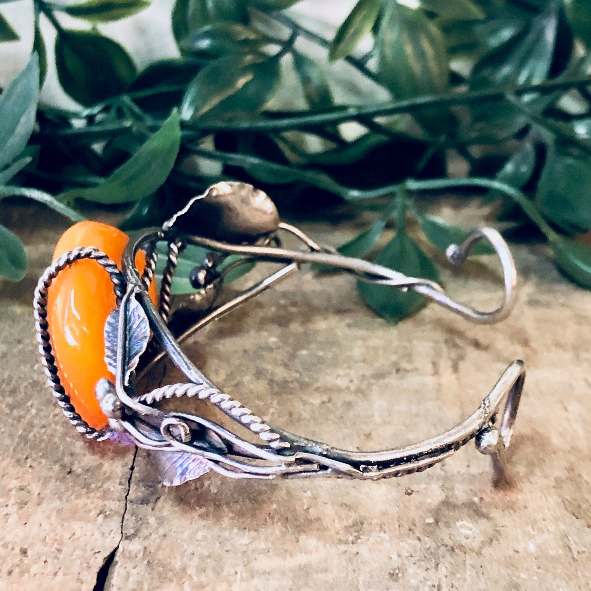 Vintage butterscotch amber bracelet with leaf design on a silver cuff band, showcasing a statement piece of 925 silver jewelry on a rustic wooden surface with green foliage in the background.