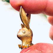 Vintage gold-toned Playboy bunny rabbit charm pendant held between fingers
