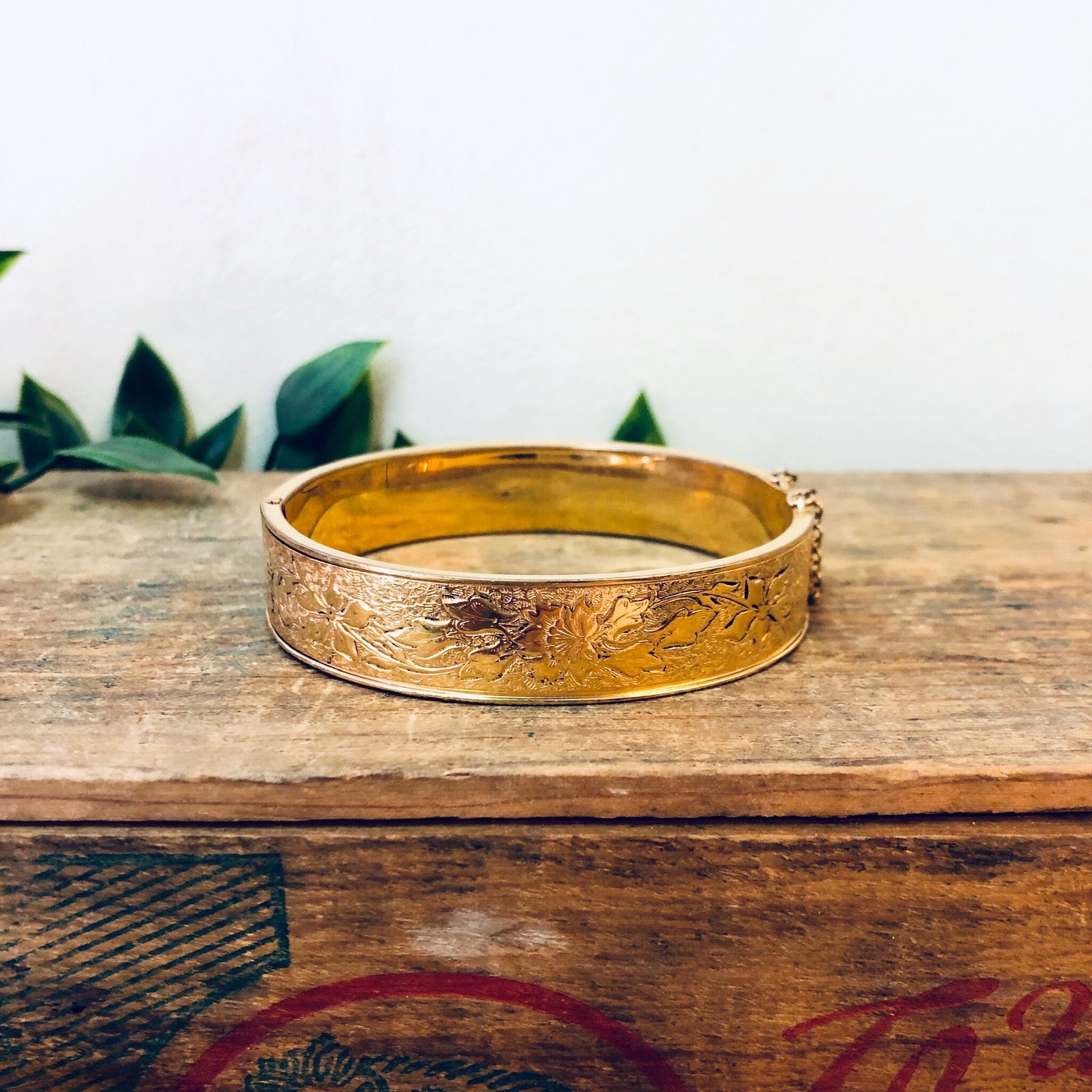 Vintage gold filled bangle bracelet with etched floral design on wooden surface with leaves in background