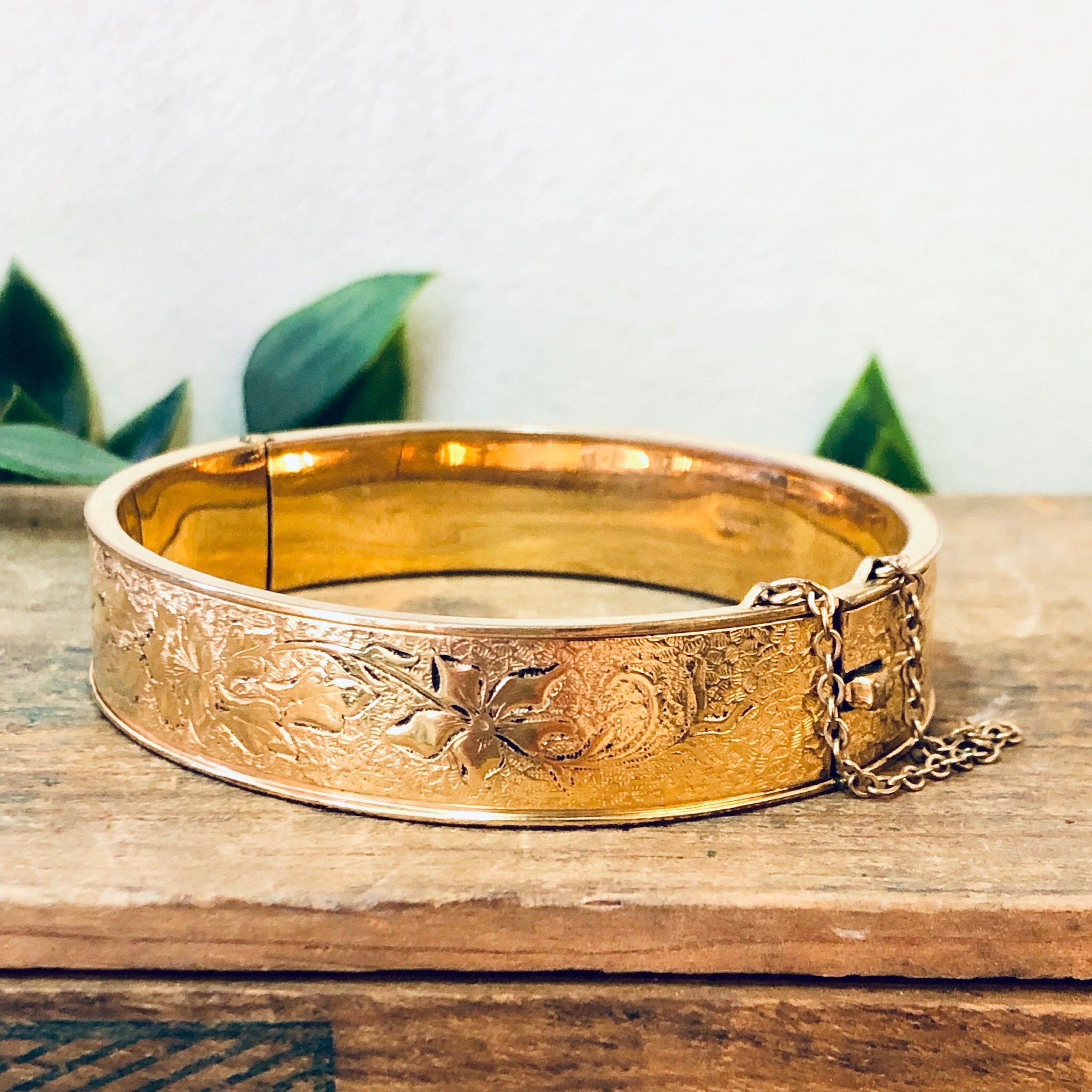 Vintage gold filled bangle bracelet with etched floral design on wooden surface with leaves in background