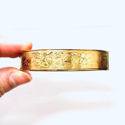 Vintage gold filled bangle bracelet with etched floral design, held in hand against white background