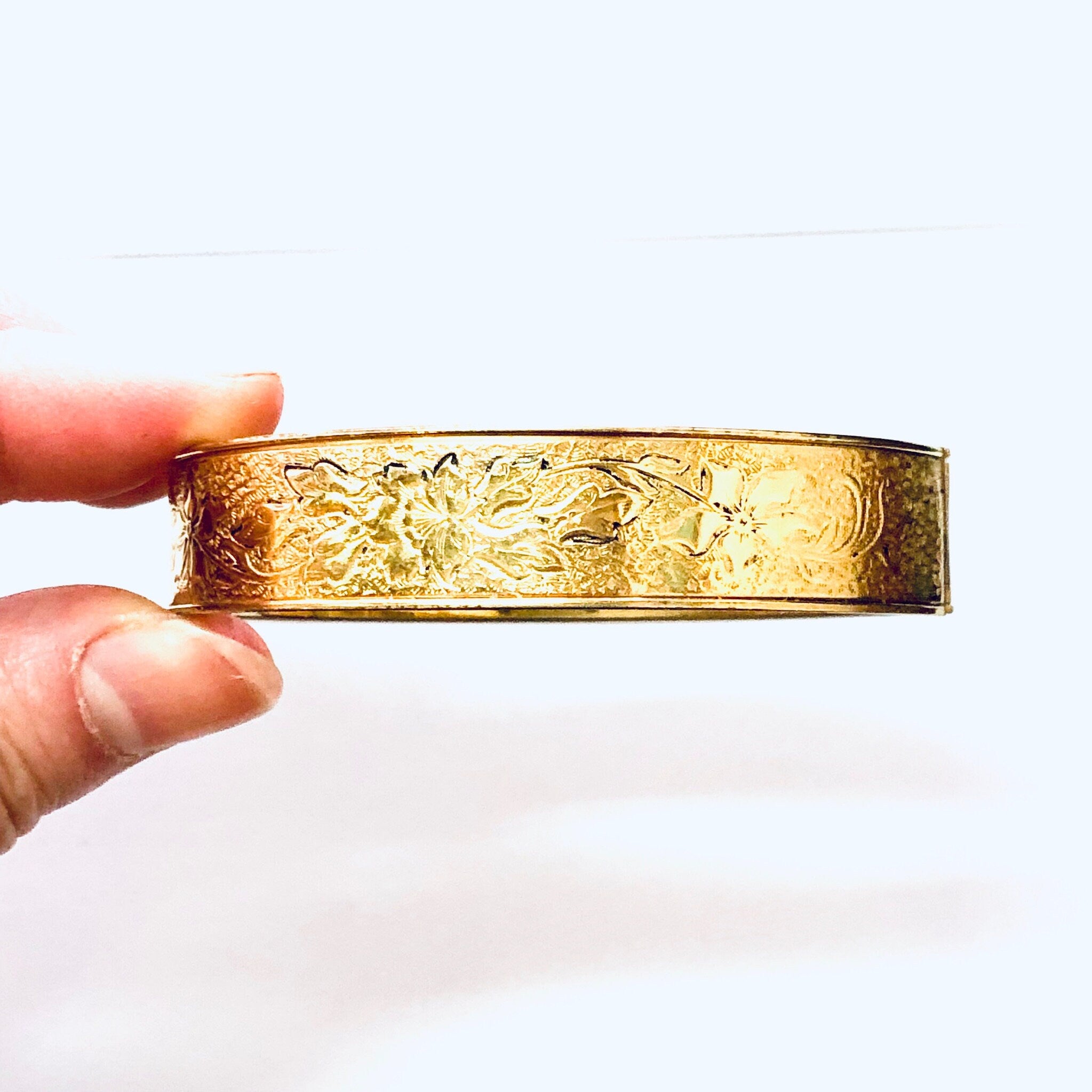 Vintage gold filled bangle bracelet with etched floral design, held in hand against white background