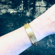 Vintage gold-filled bangle bracelet with etched floral design on wrist against dark background