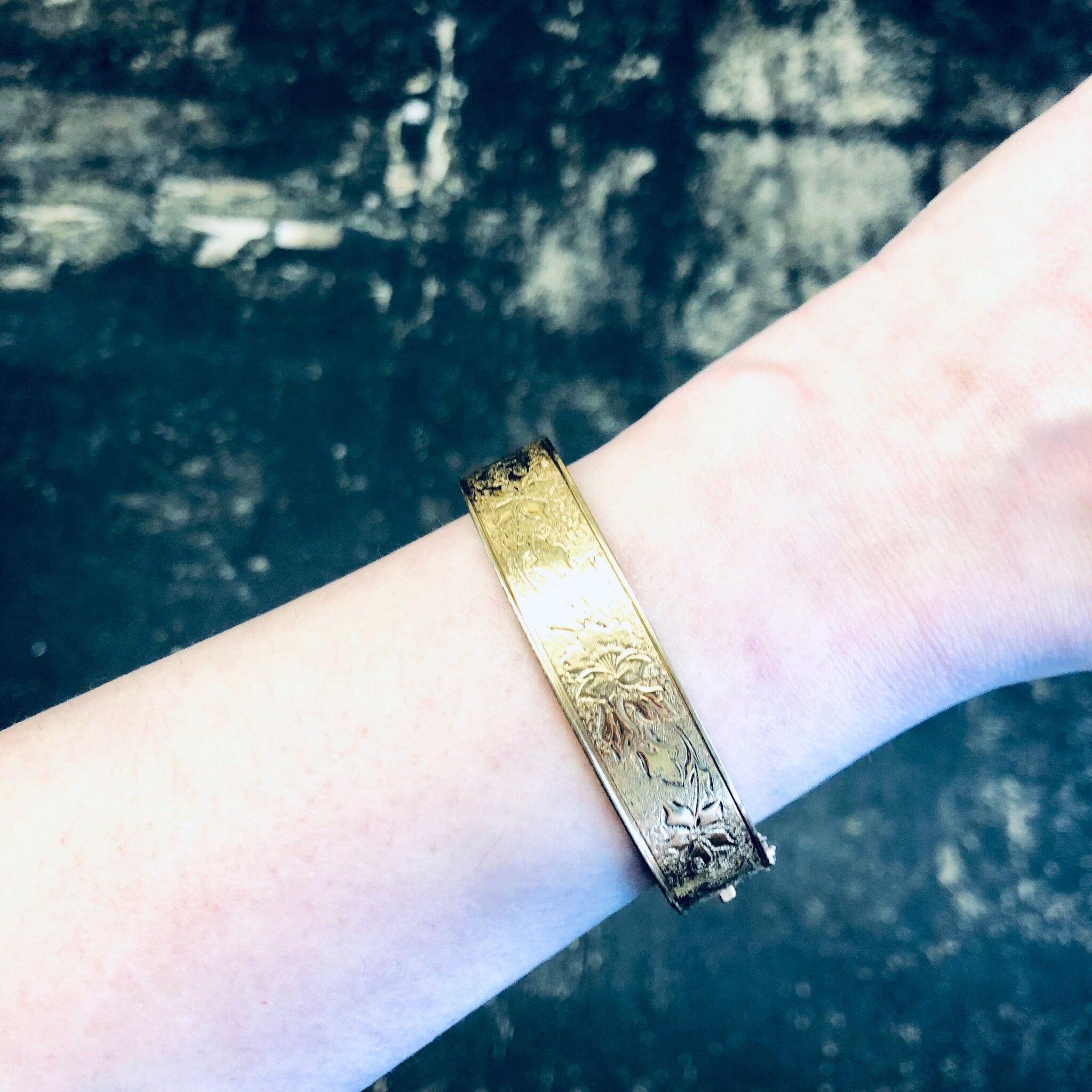 Vintage gold-filled bangle bracelet with etched floral design on wrist against dark background