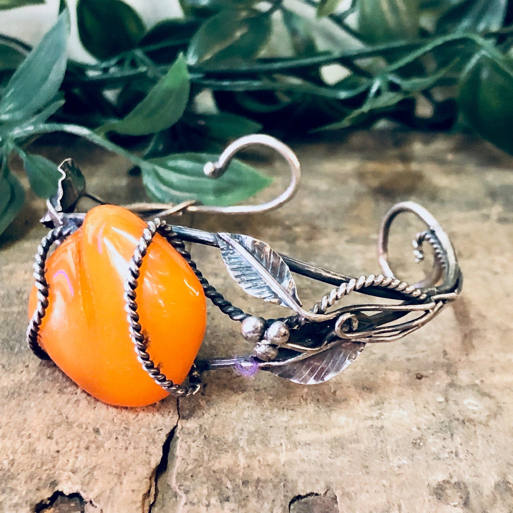 Vintage silver cuff bracelet with butterscotch amber centerpiece and leaf details, 925 sterling statement jewelry on wooden surface with green leaves in background
