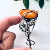 Vintage butterscotch amber cuff bracelet with silver leaf design held by a hand against a backdrop with green leaves, stamped 925 silver, statement jewelry.