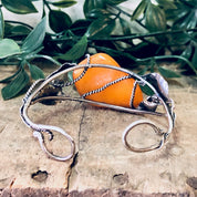 Vintage butterscotch amber silver cuff bracelet with leaf design on a wooden surface with greenery in the background, 925 stamped statement jewelry.
