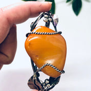 Person holding a vintage butterscotch amber and silver cuff bracelet with leaf detailing and 925 hallmark, against a white background with a hint of green foliage.