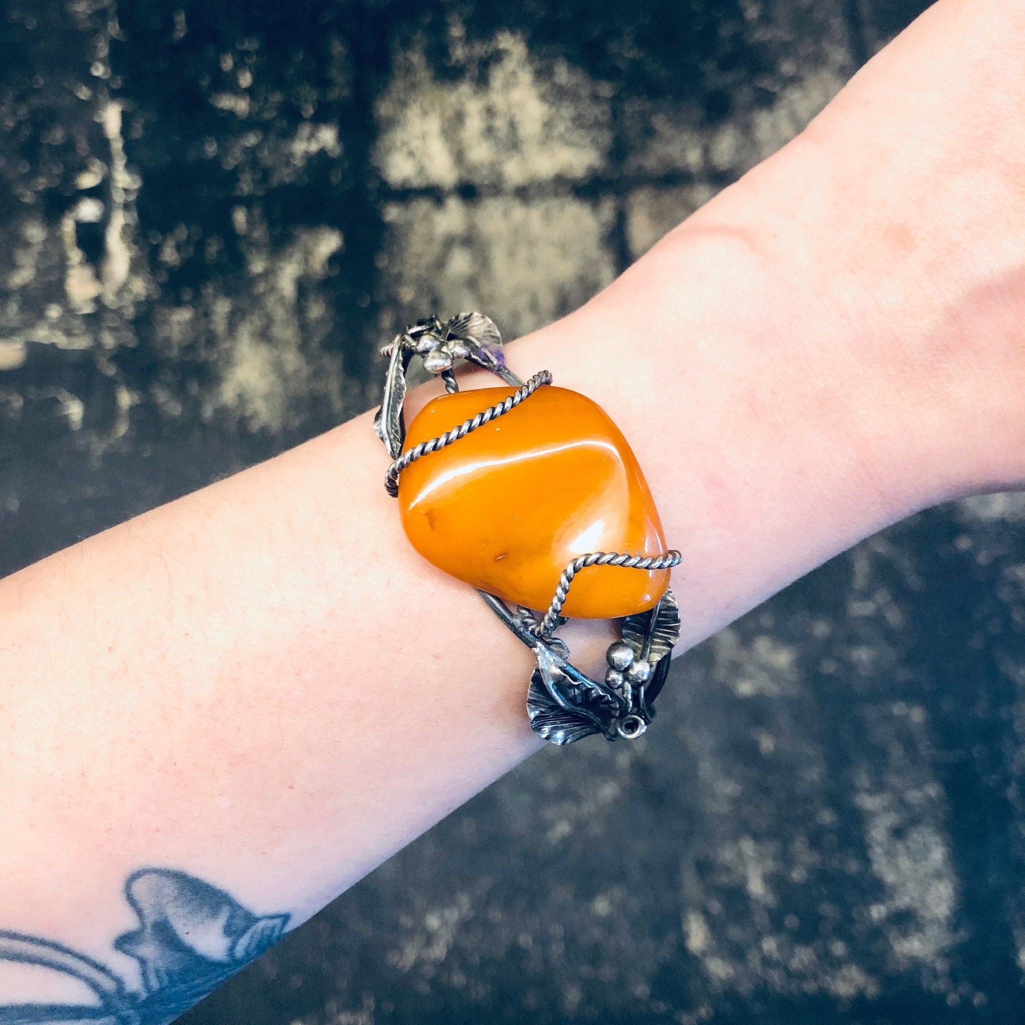 Alt text: Butterscotch amber cuff bracelet with leaf details on a wrist, showcasing a statement piece of jewelry made from 925 silver.