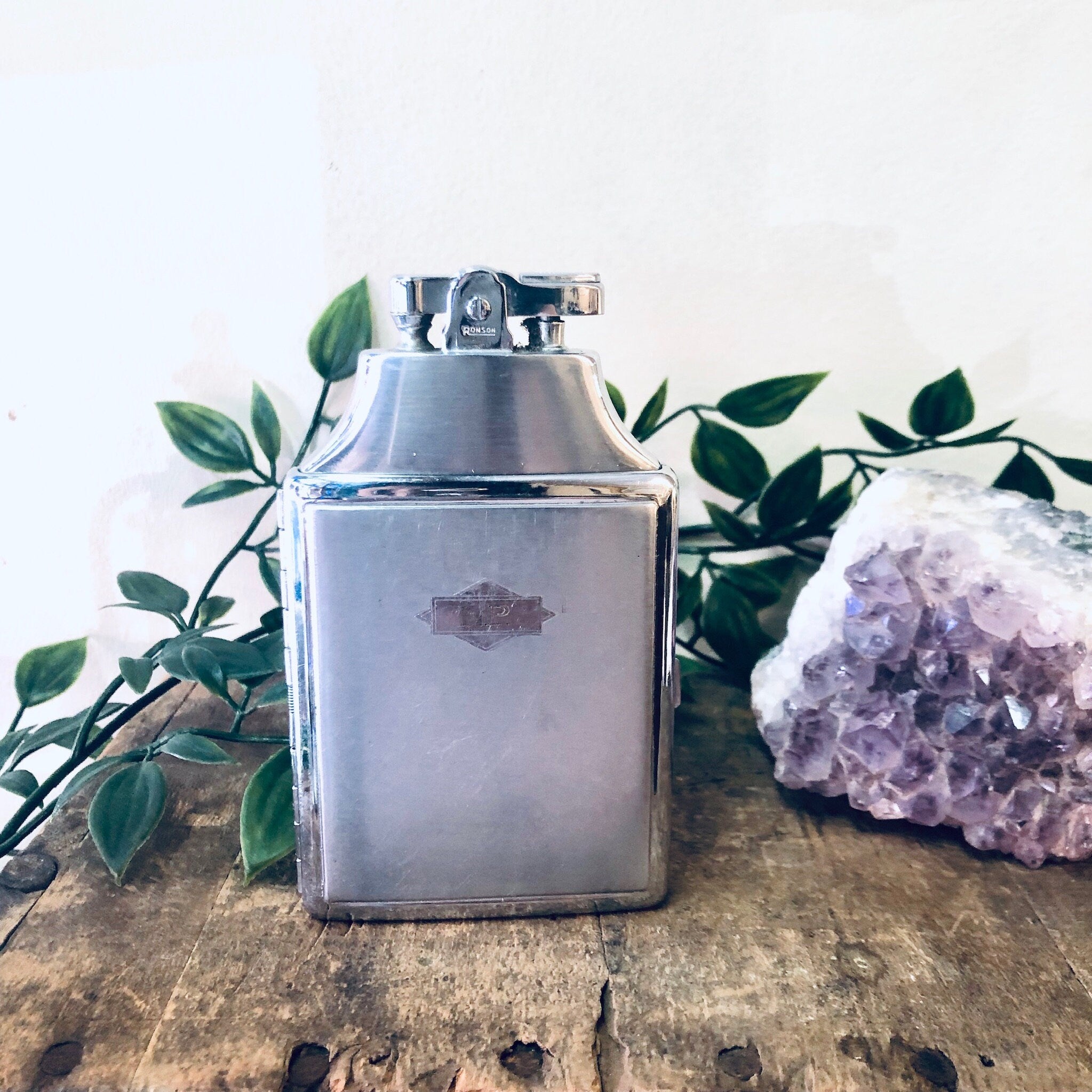 Vintage Ronson silver cigarette lighter case on wooden surface with leaves and purple geode crystal.