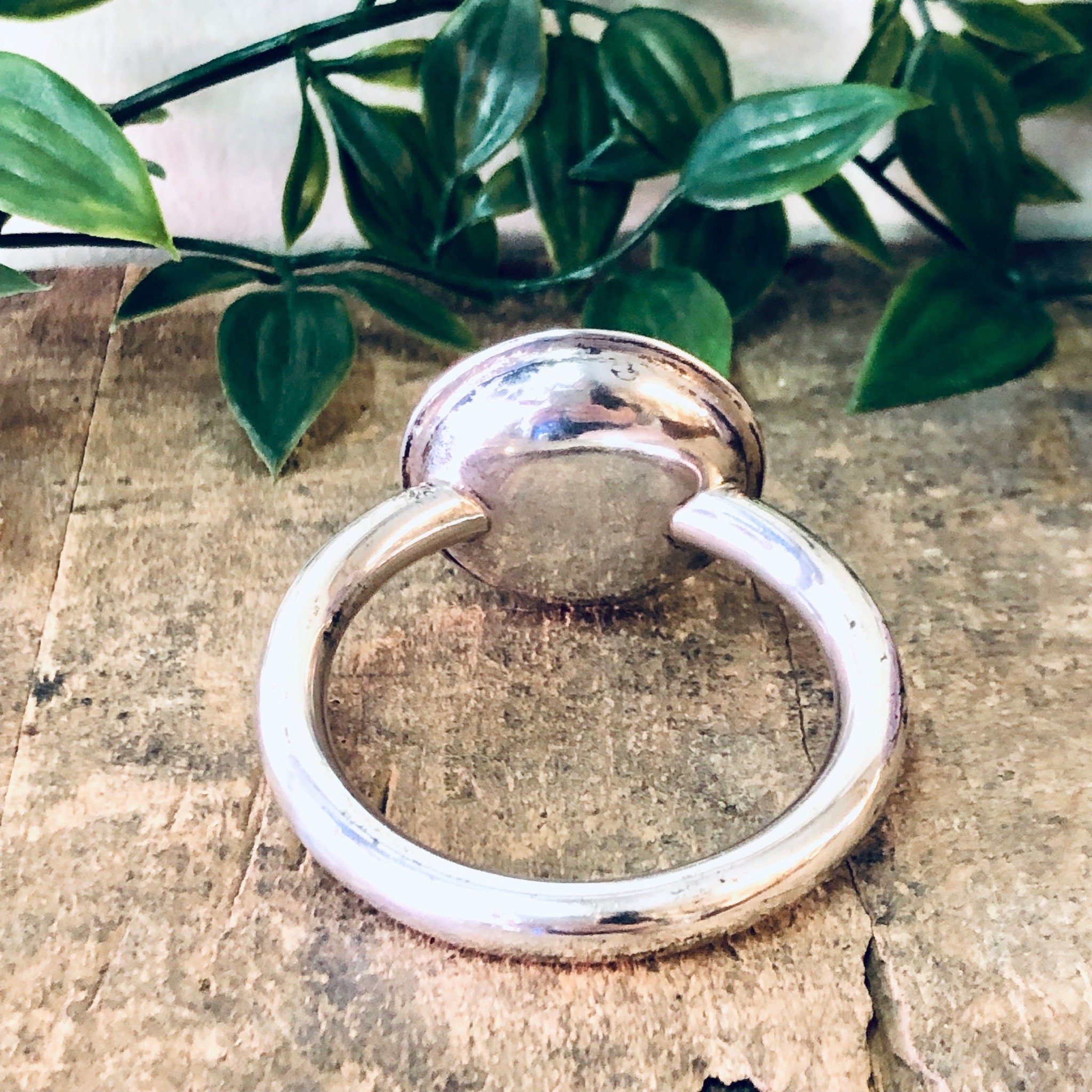 Vintage sterling silver baby rattle by Lunt on weathered wood surface with plant leaves in background