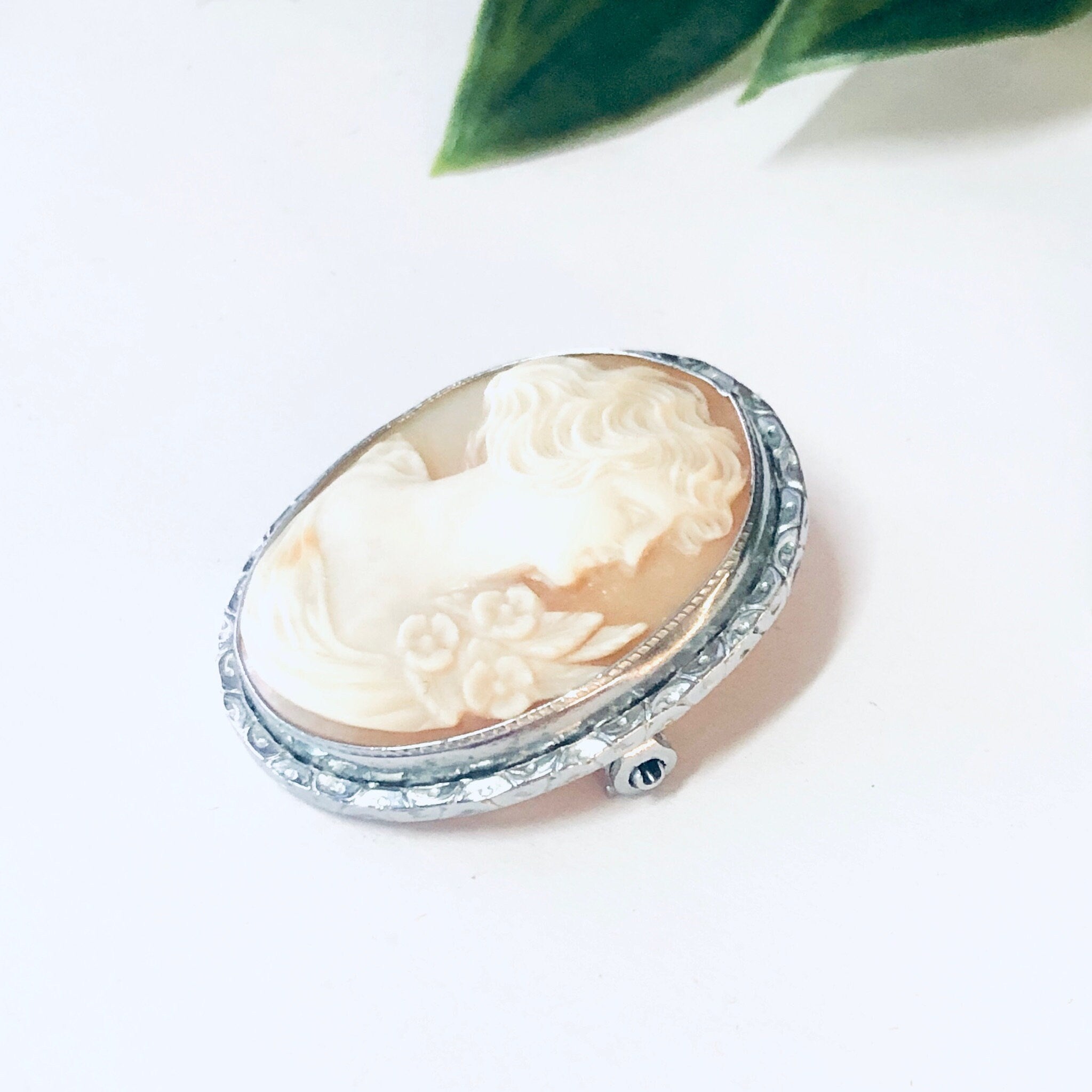 Silver vintage cameo brooch pin with intricate carved cream cameo on white background with green leaf