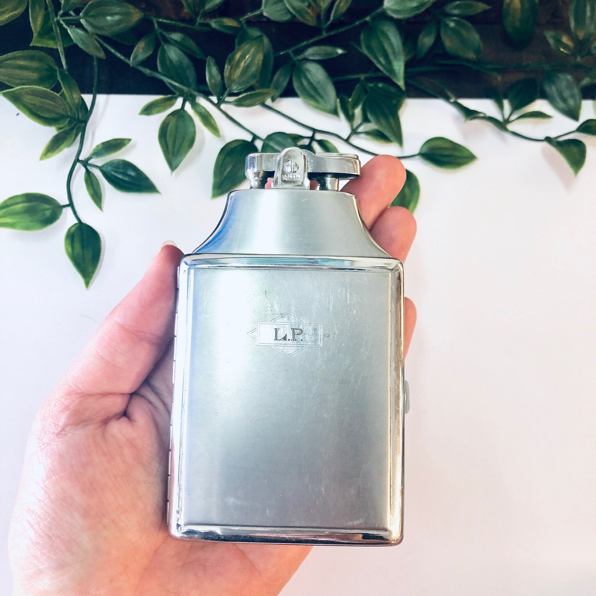 Silver Ronson vintage cigarette lighter case held in front of green foliage background