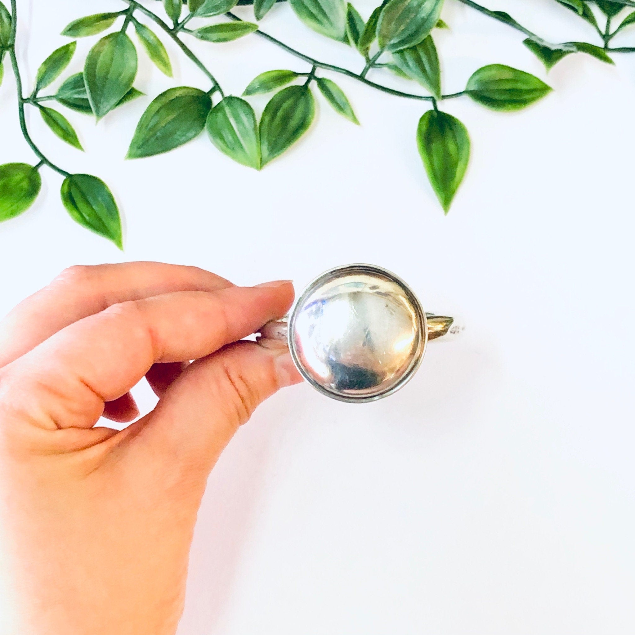 Vintage Lunt Sterling silver baby rattle held in front of green foliage on white background