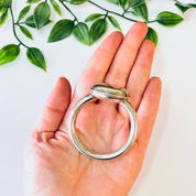 Vintage silver baby rattle from Lunt Sterling held in palm of hand with green leaves in background