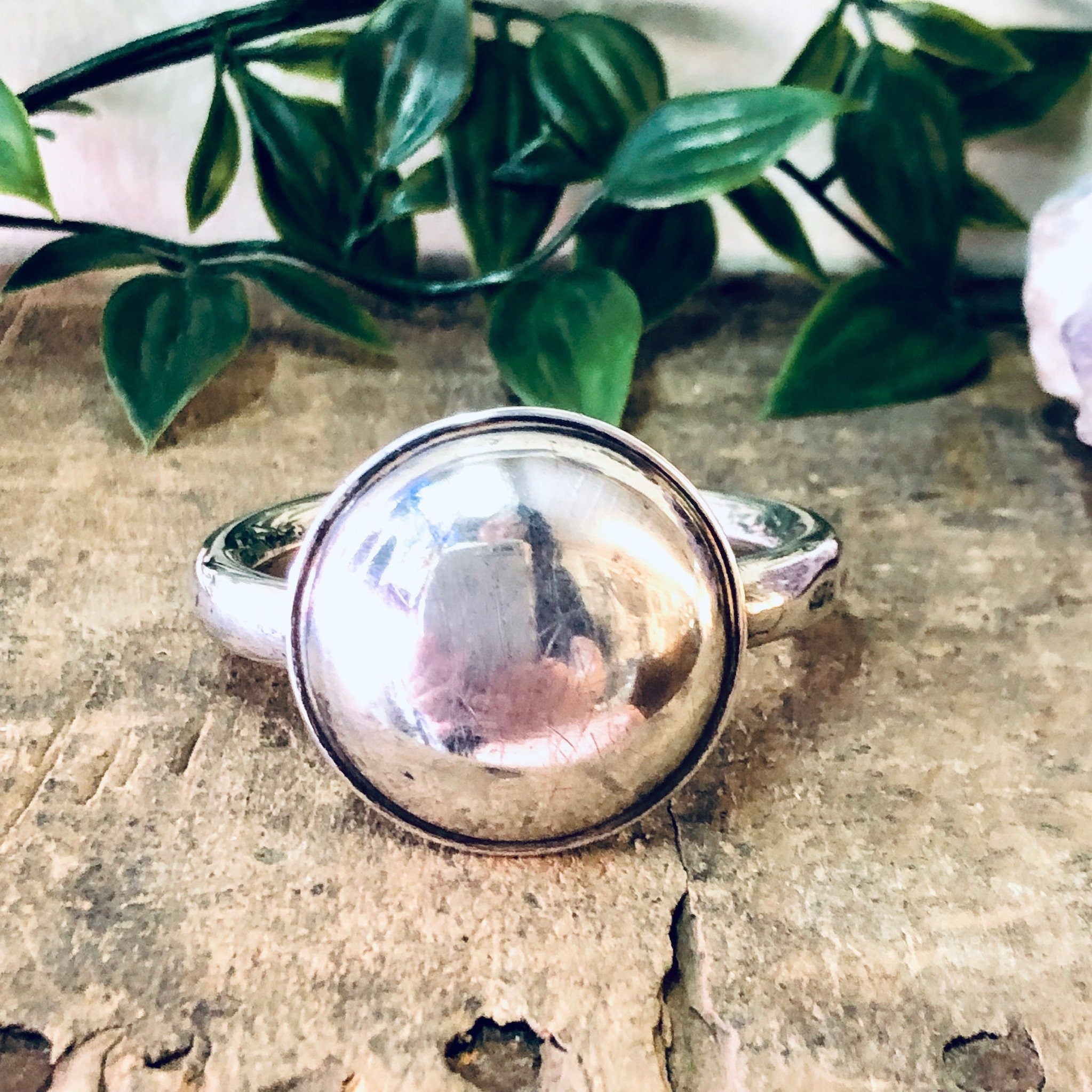 Vintage Lunt Sterling silver baby rattle on rustic wooden surface with green leaves in background