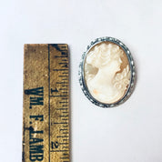 Vintage silver-toned cameo brooch pin featuring a carved profile of a Victorian woman, displayed next to an antique wooden ruler for scale.