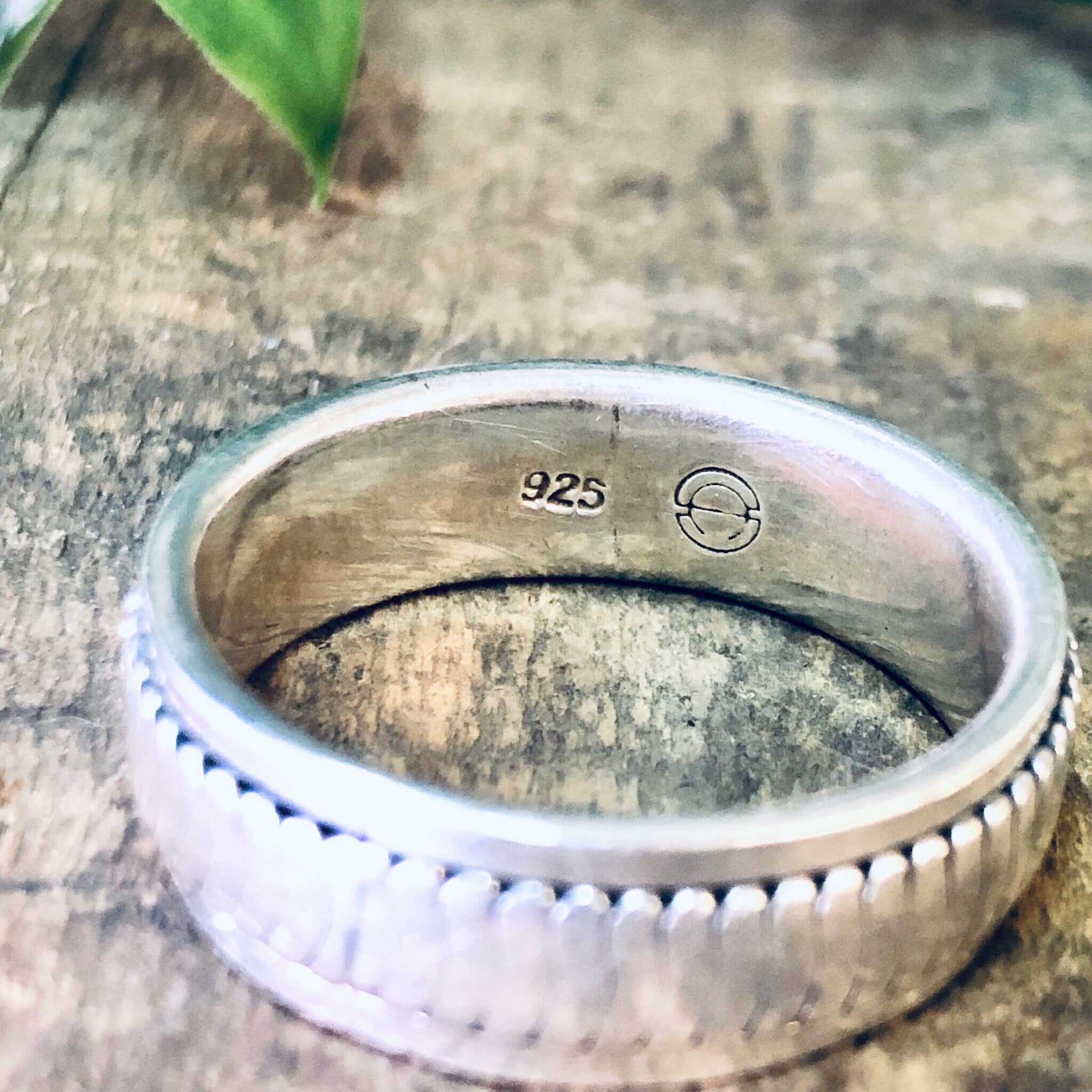 Vintage sterling silver spinner meditation ring with 925 hallmark engraved on the inside, photographed on a weathered wooden surface.