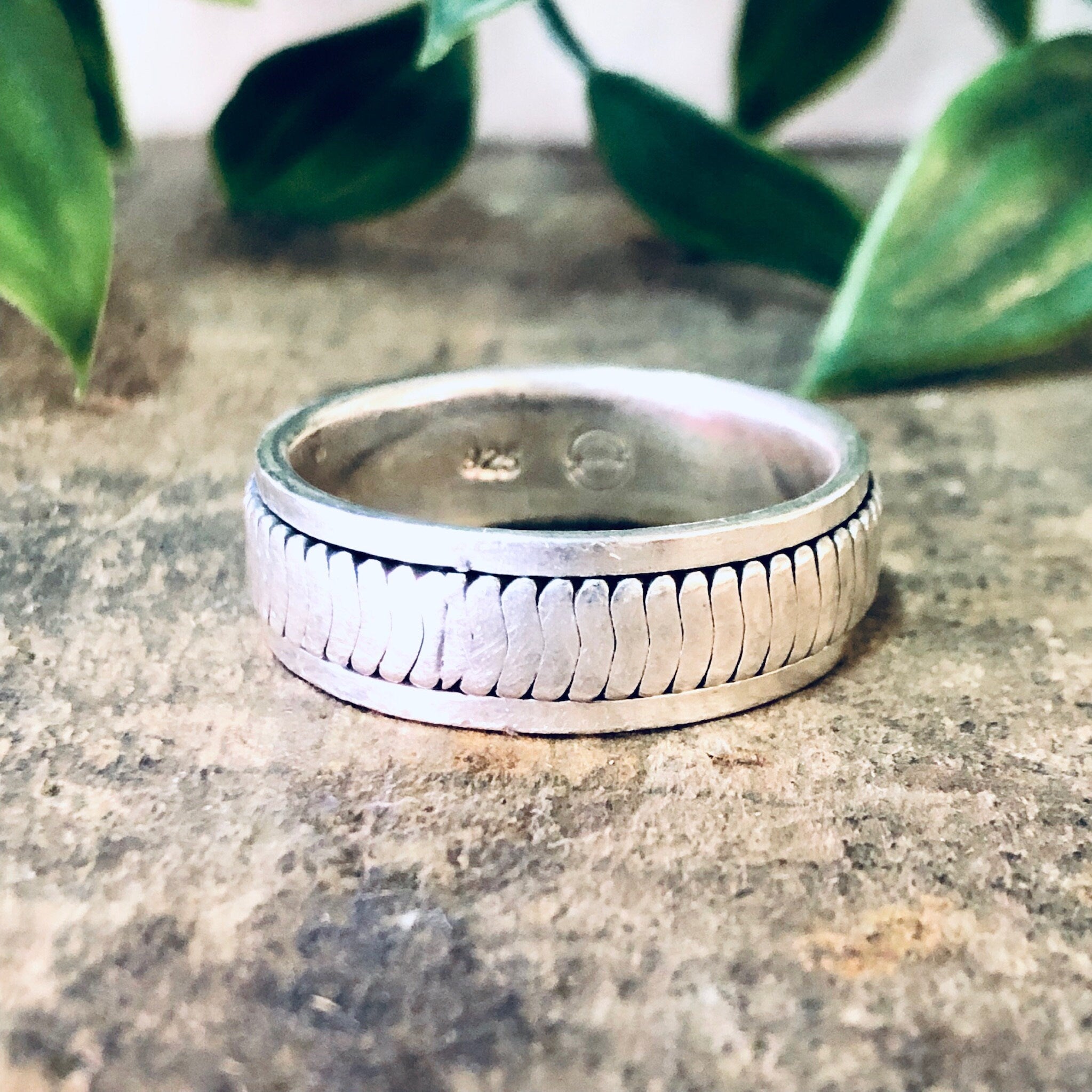 Vintage silver spinner meditation ring with textured band design, placed on stone surface with plant leaves in background