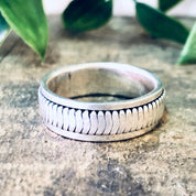 Alt text: Vintage silver spinner meditation ring with textured pattern on concrete surface with green leaves in background