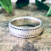 Vintage sterling silver spinner meditation ring with textured pattern, placed on weathered concrete surface with green leaves in background