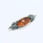 Vintage amber and silver brooch featuring an oval amber cabochon set in an ornate silver floral frame, perfect as a unique accessory or gift for lovers of vintage amber jewelry.