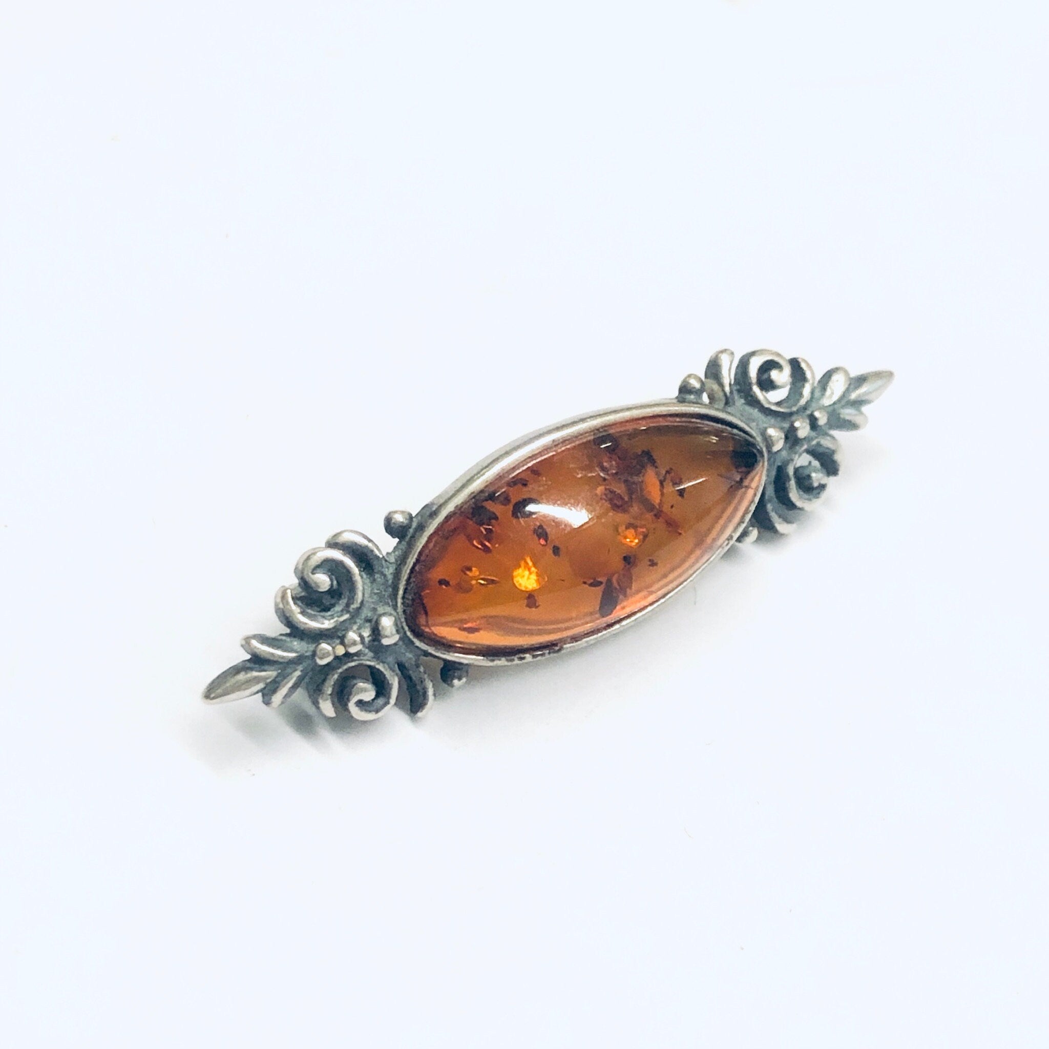 Vintage amber and silver brooch featuring an oval amber cabochon set in an ornate silver floral frame, perfect as a unique accessory or gift for lovers of vintage amber jewelry.