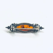 Vintage silver brooch with orange amber gemstone, ornate scrollwork design, small decorative pin jewelry.