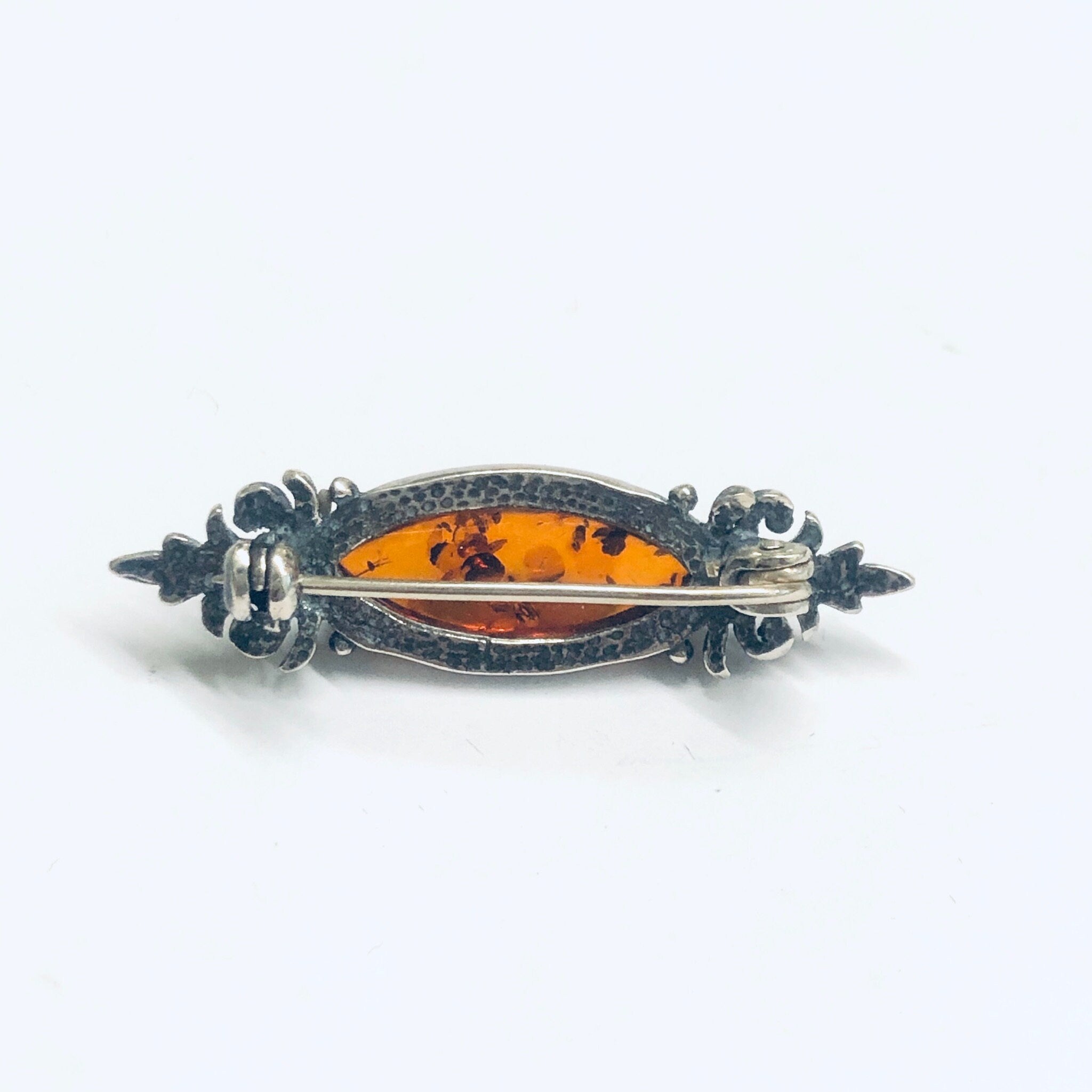 Vintage silver brooch with orange amber gemstone, ornate scrollwork design, small decorative pin jewelry.