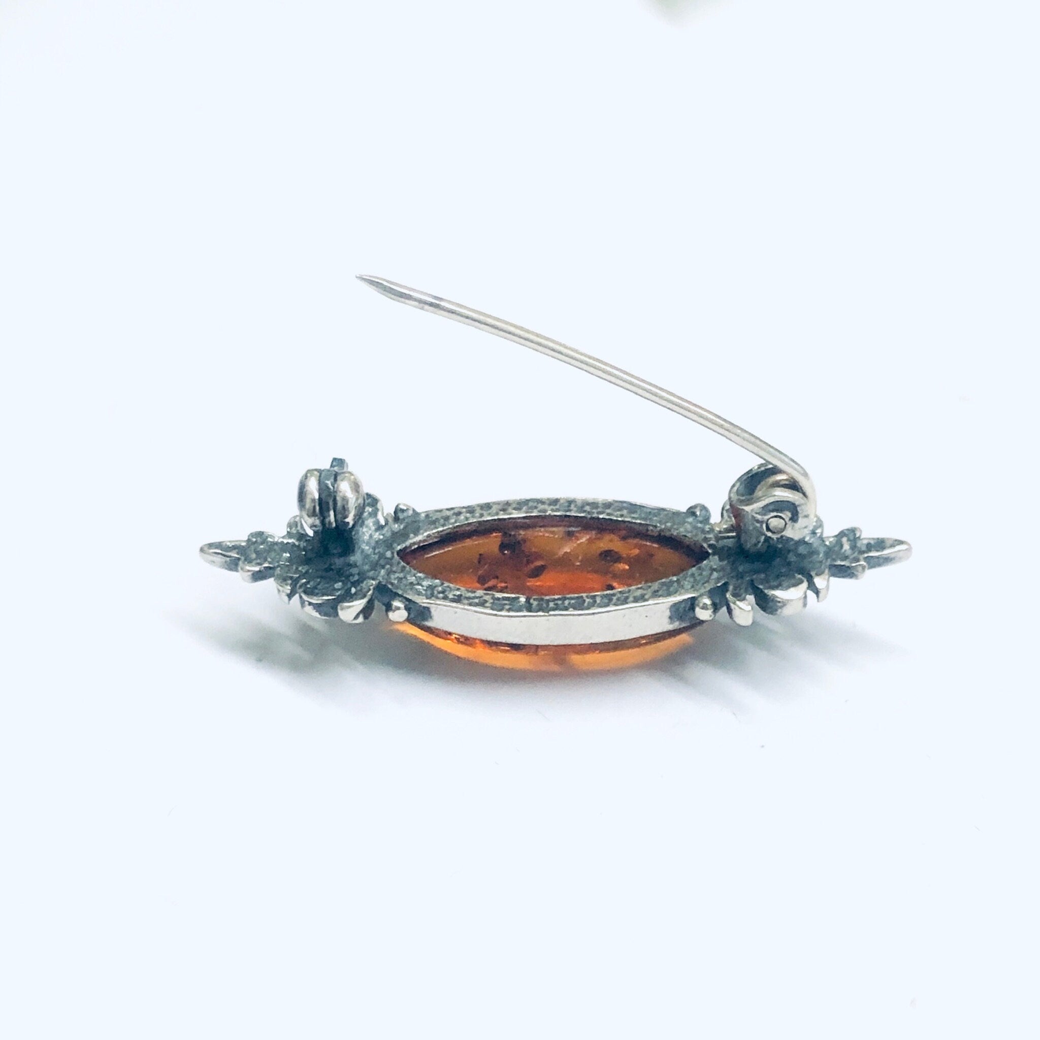 Vintage amber and silver brooch featuring an oval amber cabochon set in an ornate silver setting with floral and scroll motifs, crafted as a small, unique pin for a touch of antique elegance.