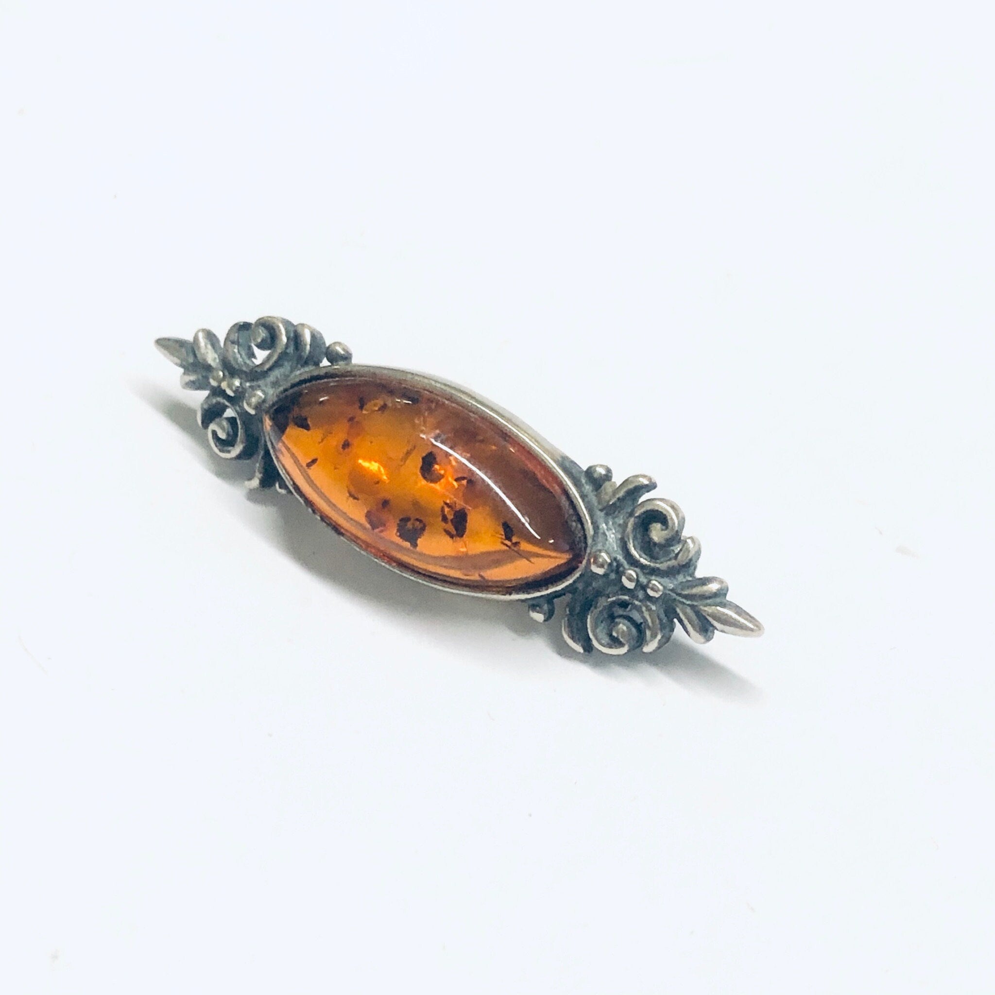 Vintage amber and silver rose brooch pin with intricate floral design and oval-shaped amber stone centerpiece, set against a plain white background.
