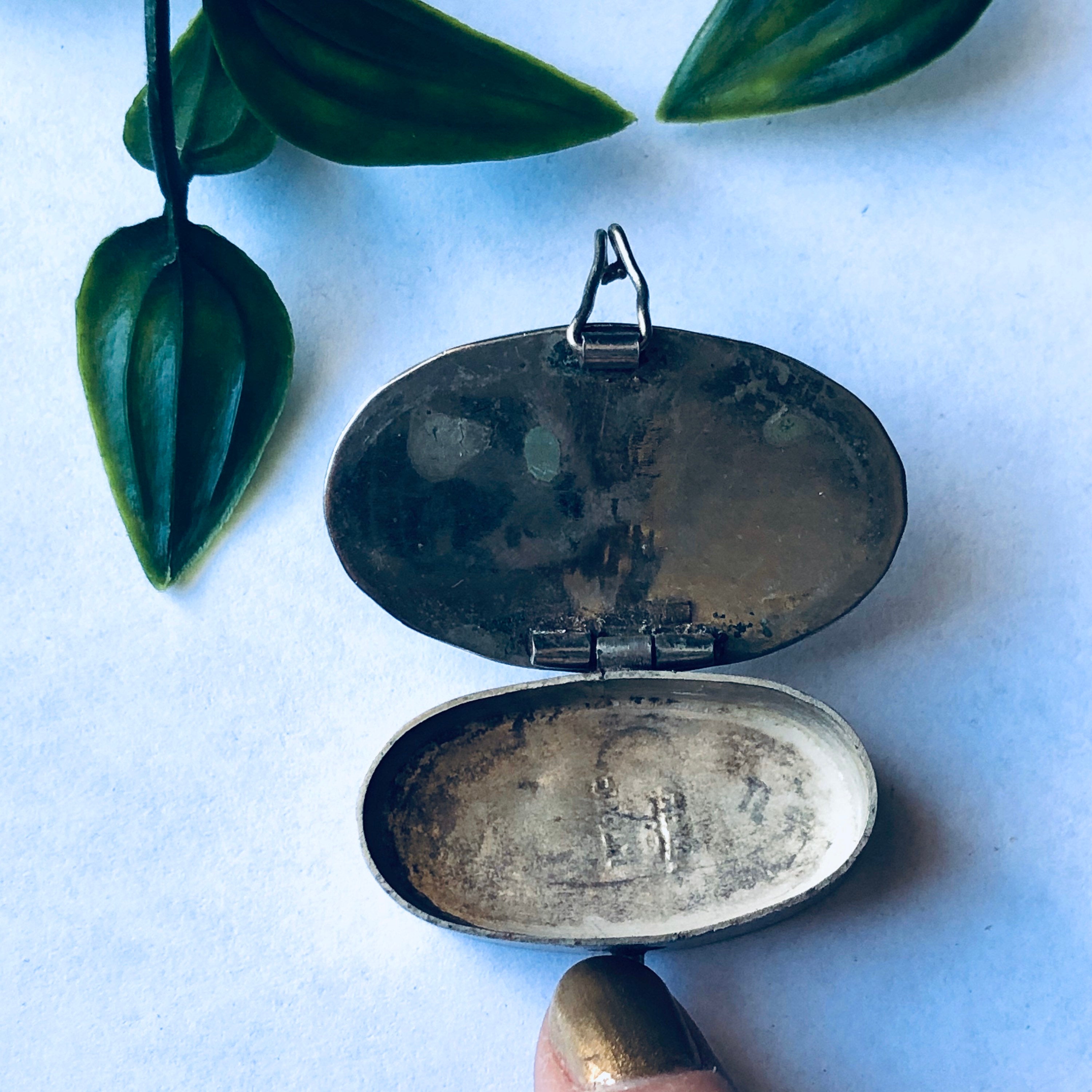 Vintage silver pill box with abalone shell inlay, blue and green shell colors, small oval shape, shown open with leaves in background.