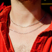 Vintage sterling silver Figaro chain necklace, approximately 34 inches long, worn around the neck of a person in a red top. The chain features thick and thin interlocking links in a classic Figaro style, made in Italy from 925 sterling silver. The extra long length allows the necklace to be layered or worn alone as a statement piece.