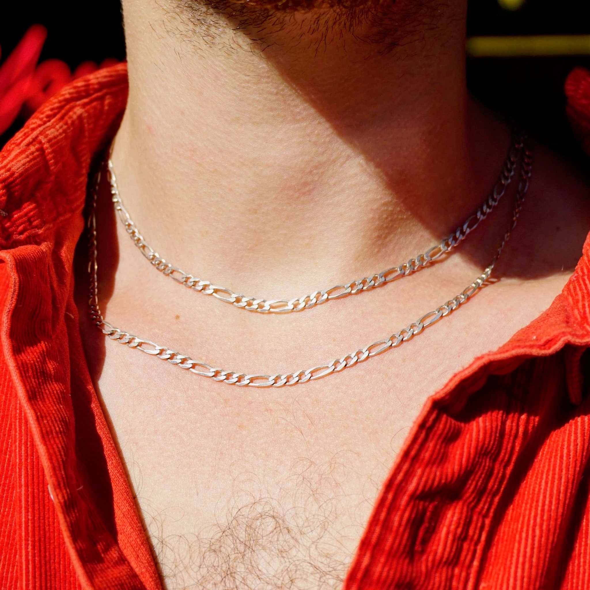 Vintage sterling silver Figaro chain necklace, approximately 34 inches long, worn around the neck of a person in a red top. The chain features thick and thin interlocking links in a classic Figaro style, made in Italy from 925 sterling silver. The extra long length allows the necklace to be layered or worn alone as a statement piece.