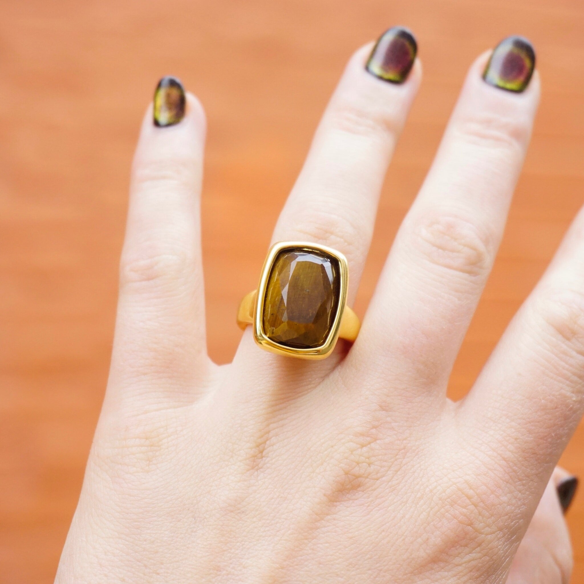 Vintage 14K gold tigers eye ring with large rectangular-cut stone on model's hand against orange background, 14K gold over resin tigers eye ring made by Milor in Italy.