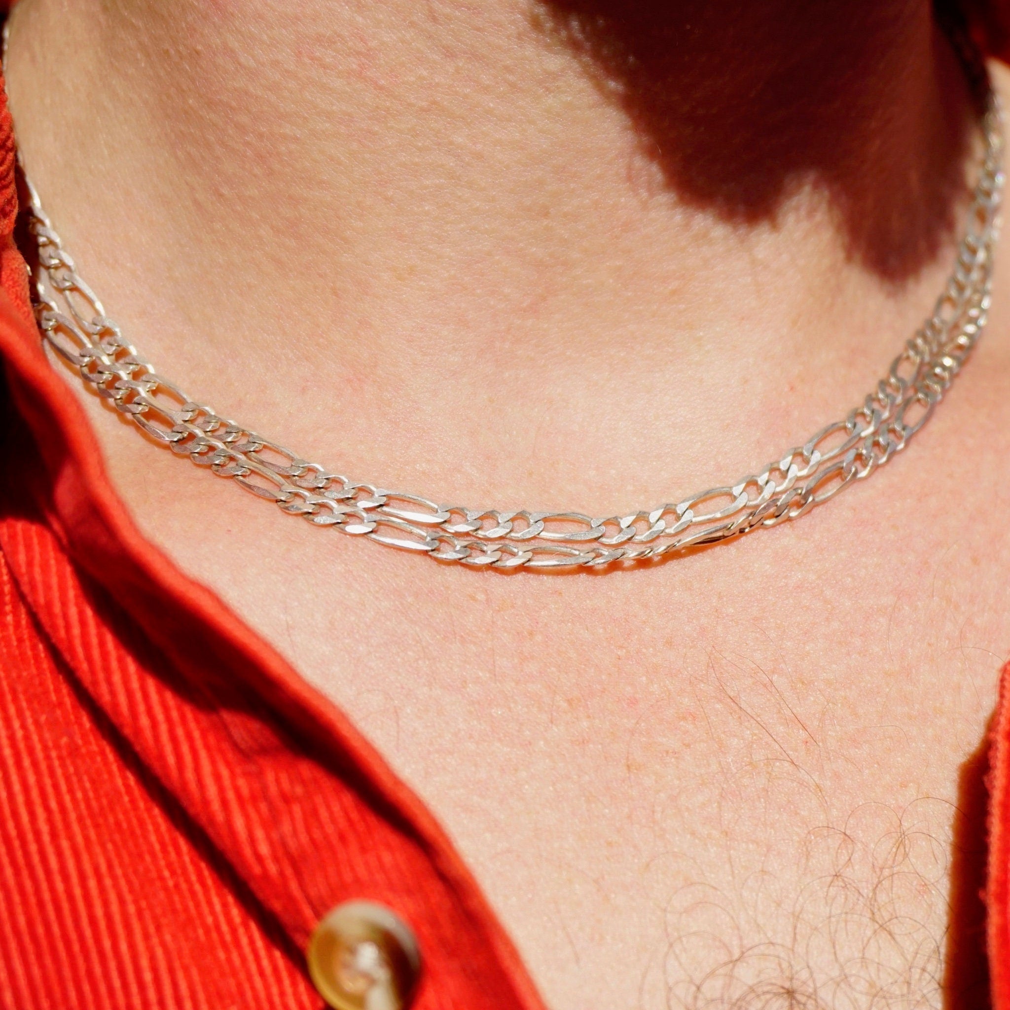 Close-up view of a person wearing a vintage sterling silver Figaro chain necklace that is extra long at 34 inches, made in Italy, and layered with a red top. The chain is hallmarked 925 indicating sterling silver purity.